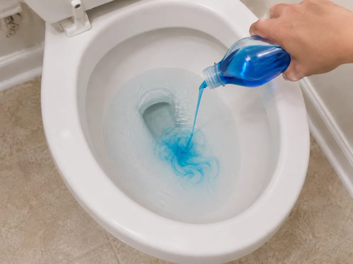 Liquid dish soap being poured into a toilet bowl to loosen a clog